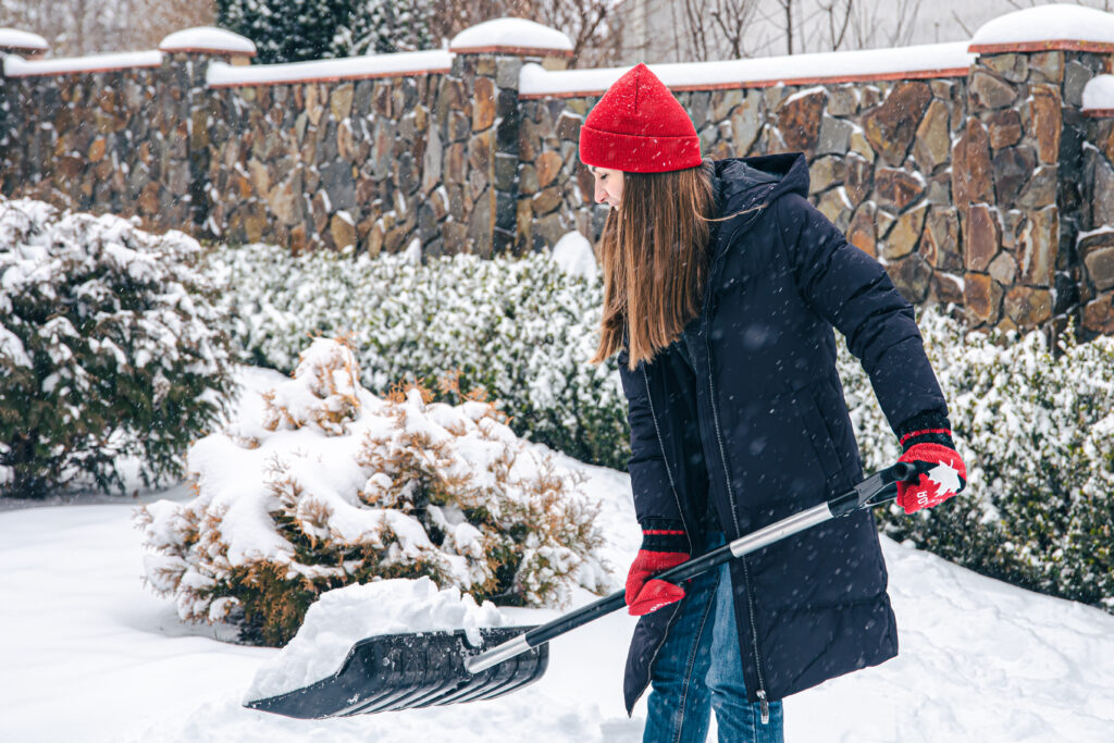 Young woman cleans snow in the yard in snowy weather.